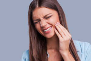 Beautiful young woman suffering from toothache while standing against grey background